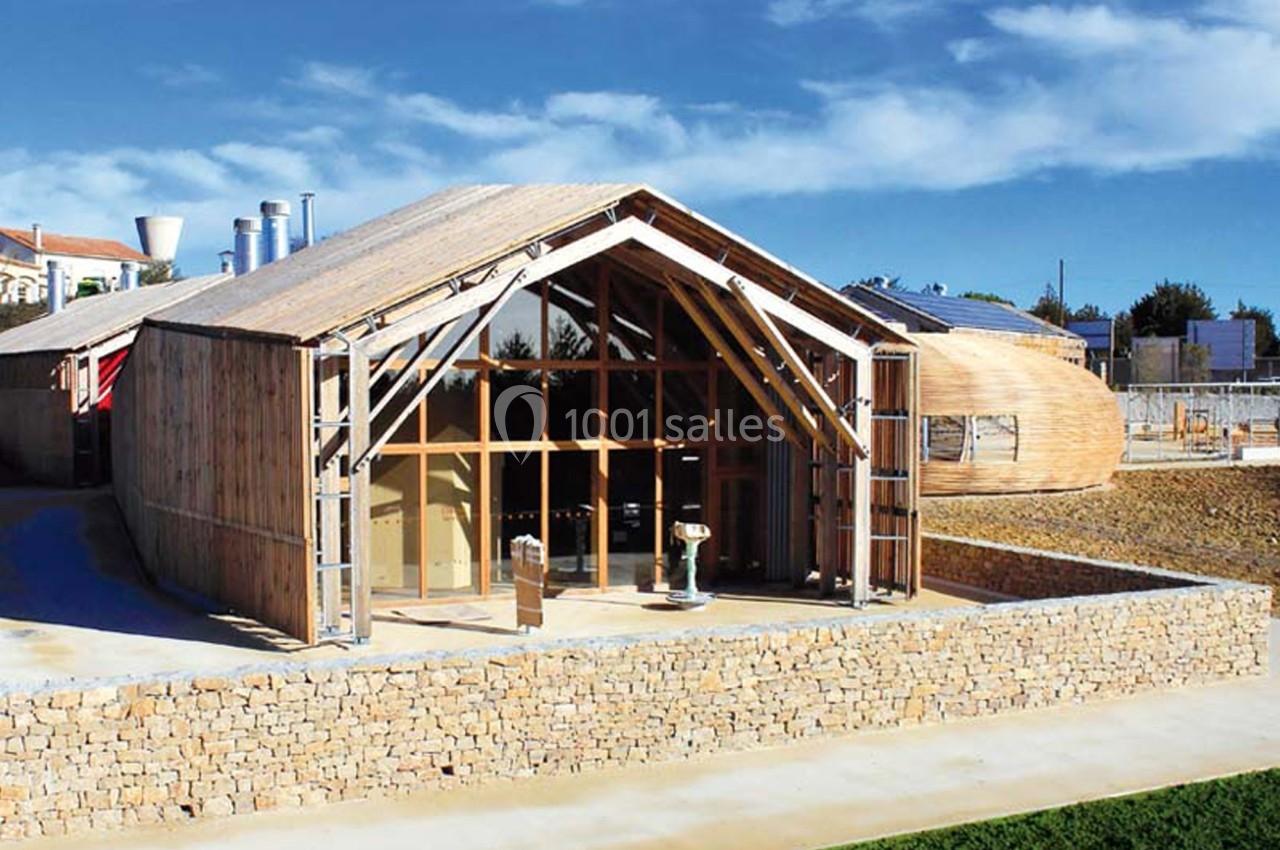 Bâtiment en bois à l'architecture moderne avec de grandes baies vitrées, entouré d'un mur en pierre et d'un espace dégagé.
