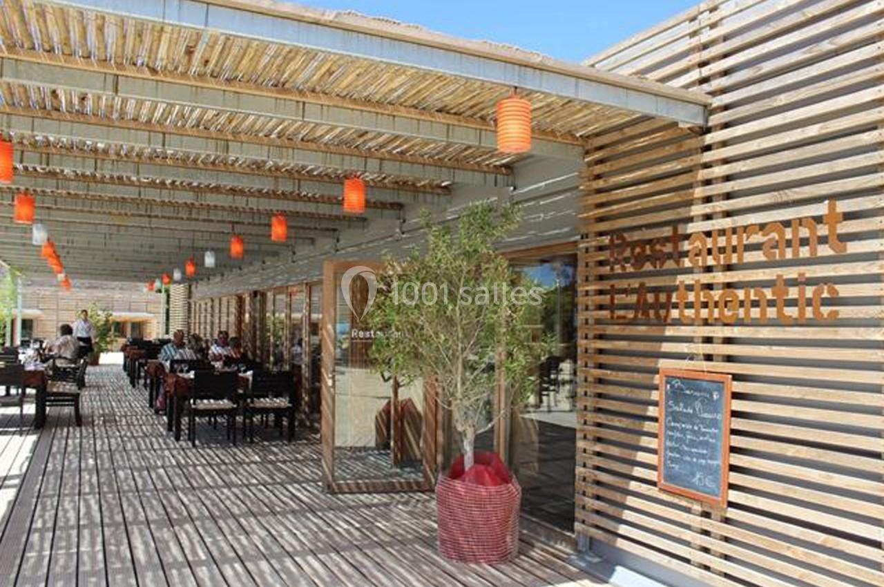 Terrasse d'un restaurant avec pergola en bois, lanternes suspendues et tables dressées pour les clients.