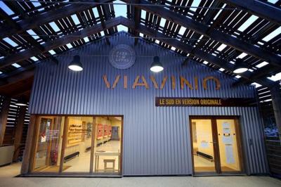 Salle de réunion lumineuse avec tables en U, chaises en bois, tonneau décoratif et étagères murales garnies de bouteilles.