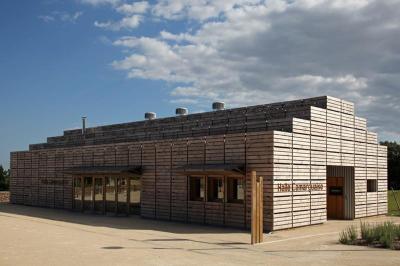 Salle de réunion lumineuse avec tables en U, chaises en bois, tonneau décoratif et étagères murales garnies de bouteilles.