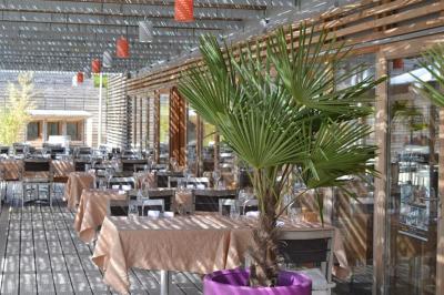 Salle de réunion lumineuse avec tables en U, chaises en bois, tonneau décoratif et étagères murales garnies de bouteilles.