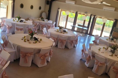 Salle de réunion lumineuse avec tables en U, chaises en bois, tonneau décoratif et étagères murales garnies de bouteilles.