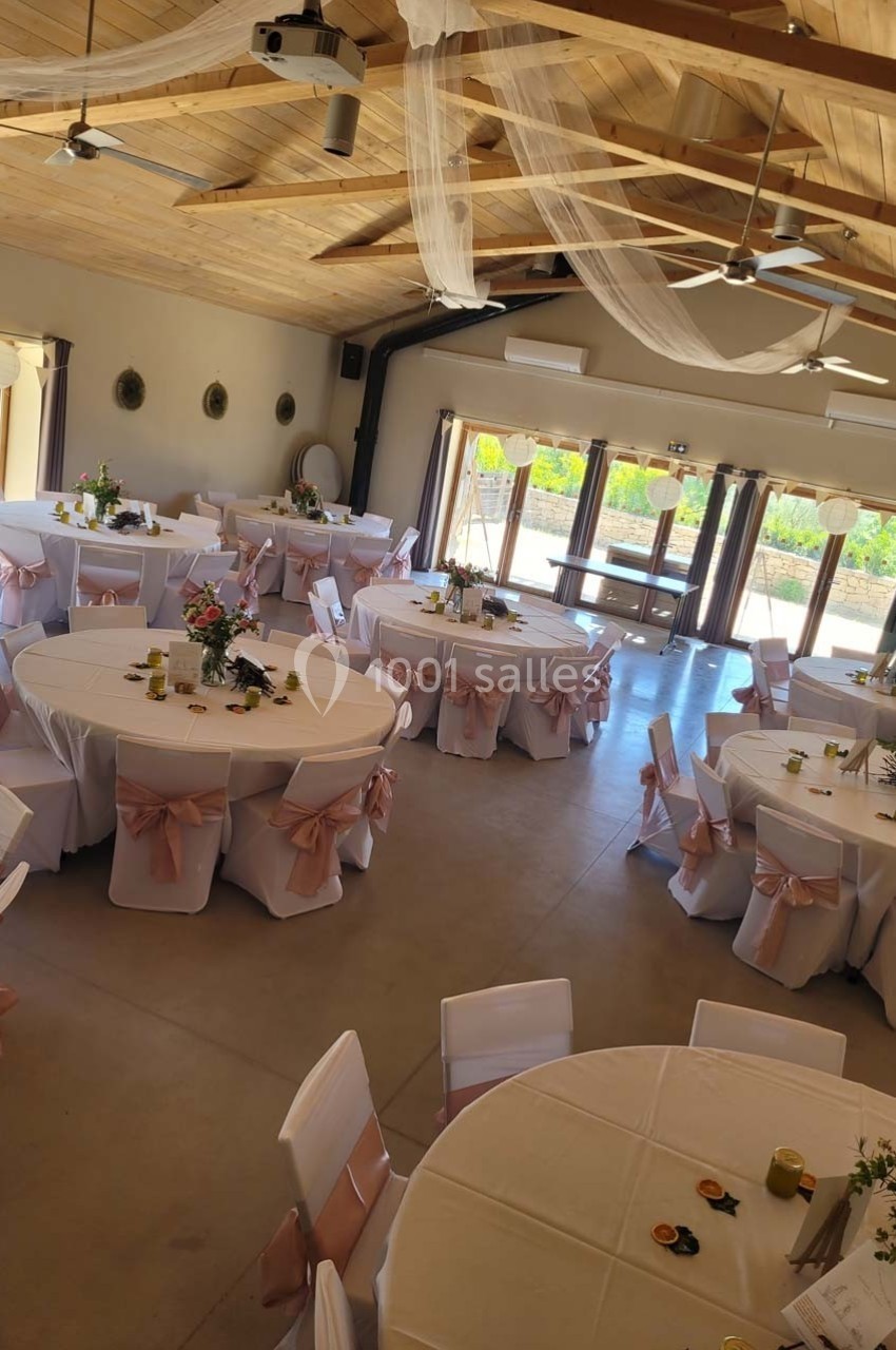Salle de réception décorée avec des tables rondes, nappes blanches et chaises ornées de nœuds roses.