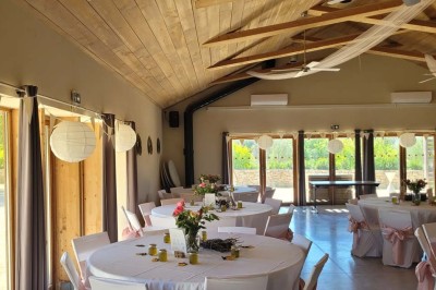 Salle de réunion lumineuse avec tables en U, chaises en bois, tonneau décoratif et étagères murales garnies de bouteilles.