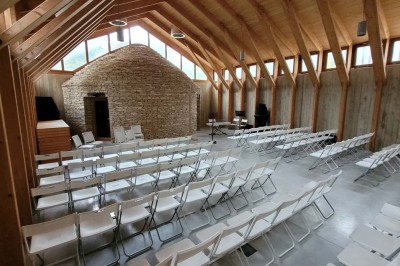 Salle de réunion lumineuse avec tables en U, chaises en bois, tonneau décoratif et étagères murales garnies de bouteilles.