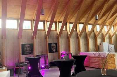 Salle de réunion lumineuse avec tables en U, chaises en bois, tonneau décoratif et étagères murales garnies de bouteilles.