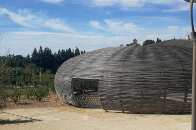 Salle de réunion lumineuse avec tables en U, chaises en bois, tonneau décoratif et étagères murales garnies de bouteilles.