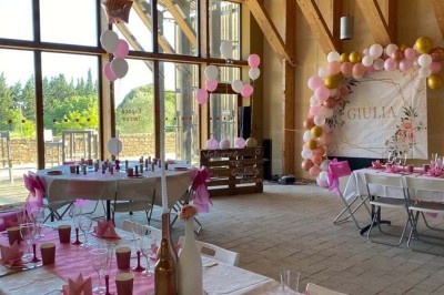Salle de réunion lumineuse avec tables en U, chaises en bois, tonneau décoratif et étagères murales garnies de bouteilles.