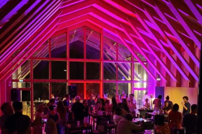 Salle de réunion lumineuse avec tables en U, chaises en bois, tonneau décoratif et étagères murales garnies de bouteilles.