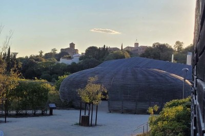 Salle de réunion lumineuse avec tables en U, chaises en bois, tonneau décoratif et étagères murales garnies de bouteilles.