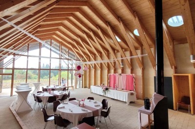 Salle de réunion lumineuse avec tables en U, chaises en bois, tonneau décoratif et étagères murales garnies de bouteilles.