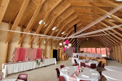Salle de réunion lumineuse avec tables en U, chaises en bois, tonneau décoratif et étagères murales garnies de bouteilles.