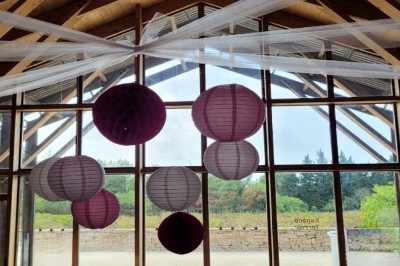 Salle de réunion lumineuse avec tables en U, chaises en bois, tonneau décoratif et étagères murales garnies de bouteilles.