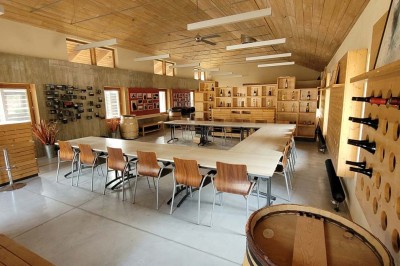 Salle de réunion lumineuse avec tables en U, chaises en bois, tonneau décoratif et étagères murales garnies de bouteilles.