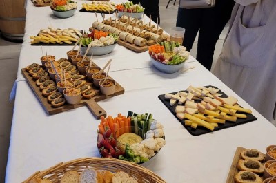 Salle de réunion lumineuse avec tables en U, chaises en bois, tonneau décoratif et étagères murales garnies de bouteilles.