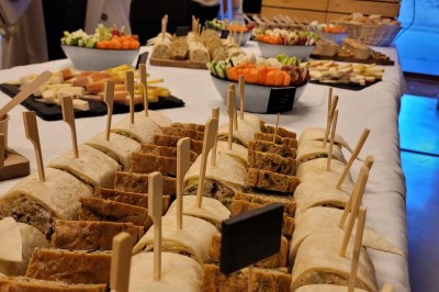 Salle de réunion lumineuse avec tables en U, chaises en bois, tonneau décoratif et étagères murales garnies de bouteilles.
