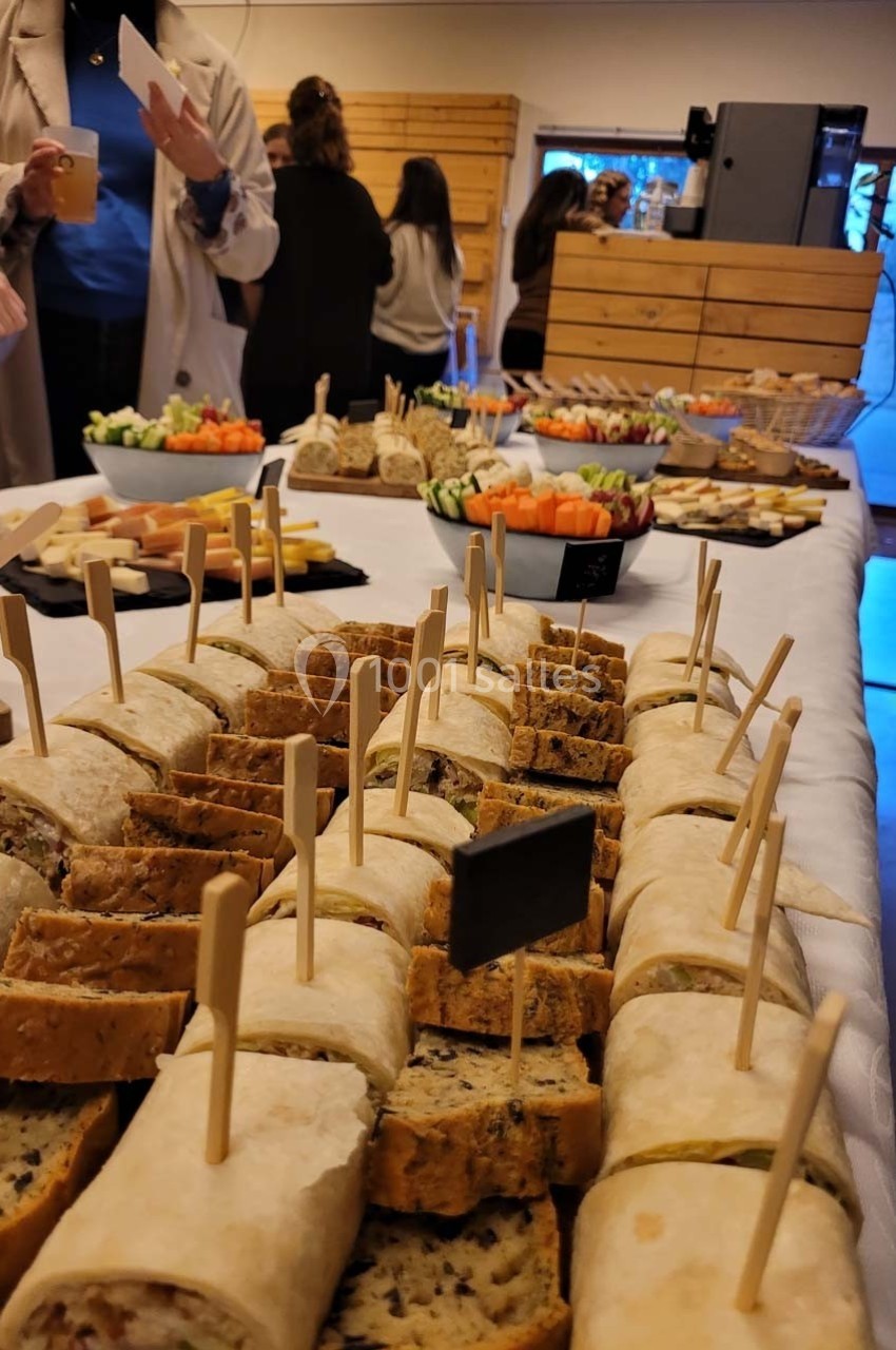 Plateau de wraps et amuse-bouches disposés sur une table lors d'un buffet, avec des invités en arrière-plan.