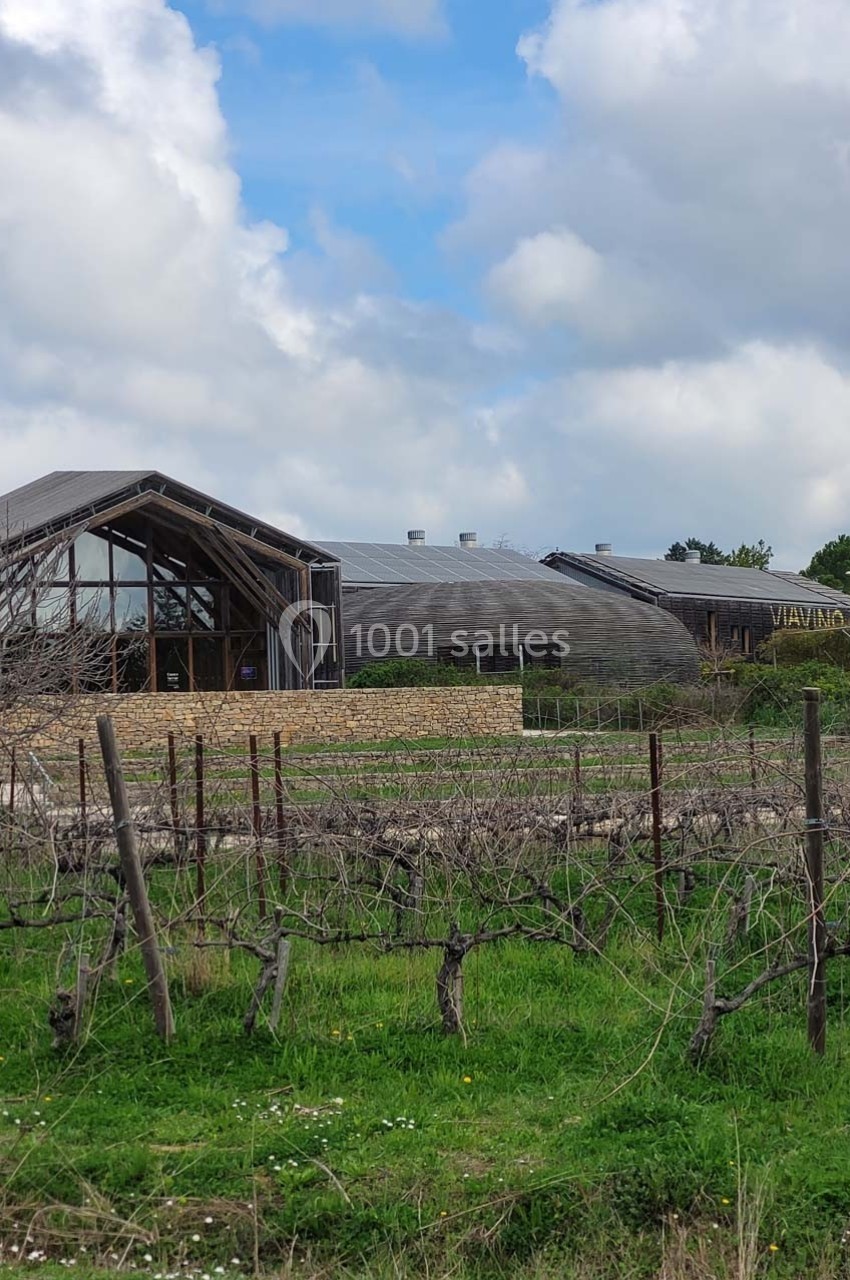 Bâtiment moderne en bois entouré de vignes et de verdure sous un ciel partiellement nuageux.