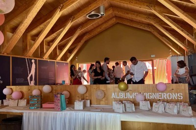 Salle de réunion lumineuse avec tables en U, chaises en bois, tonneau décoratif et étagères murales garnies de bouteilles.