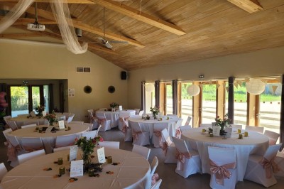 Salle de réunion lumineuse avec tables en U, chaises en bois, tonneau décoratif et étagères murales garnies de bouteilles.