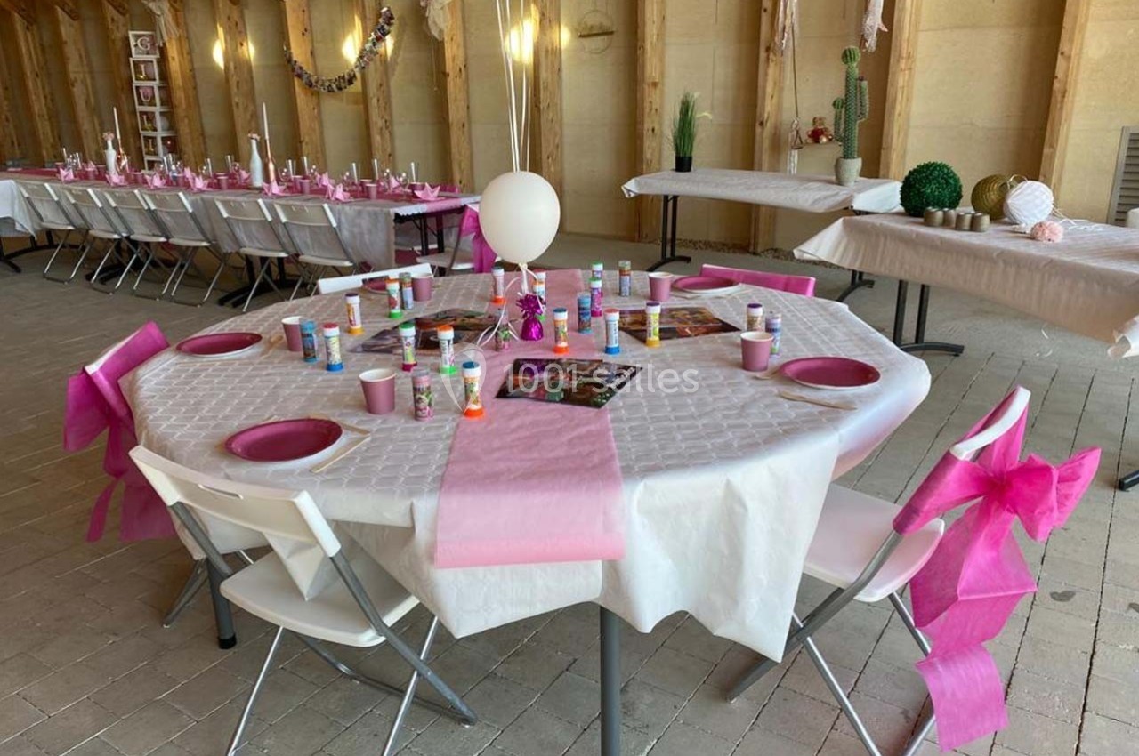Table décorée pour un événement avec nappes blanches, rubans roses, ballons et matériel créatif disposé.
