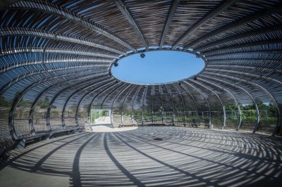 Salle de réunion lumineuse avec tables en U, chaises en bois, tonneau décoratif et étagères murales garnies de bouteilles.