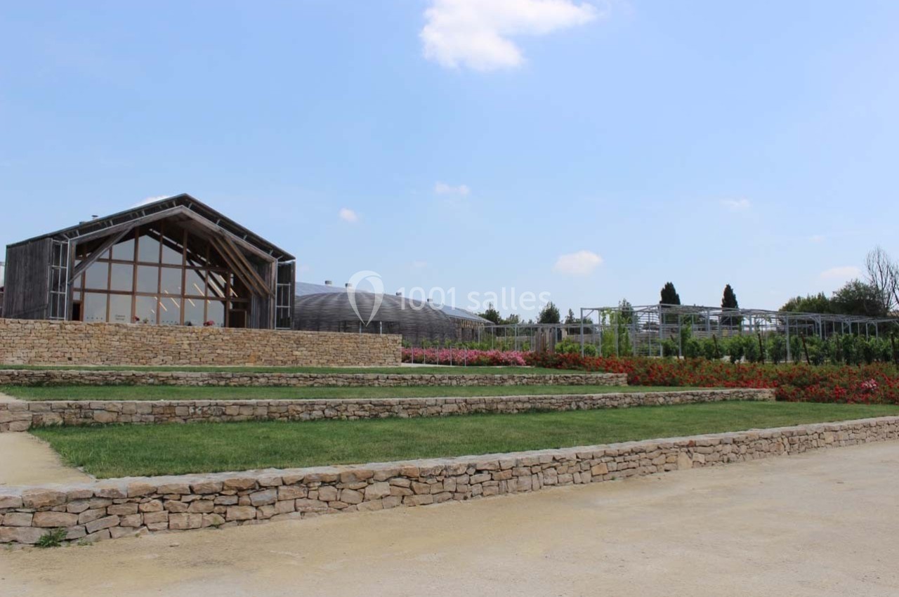 Bâtiment moderne en bois et verre entouré de jardins fleuris, avec un ciel dégagé en arrière-plan.