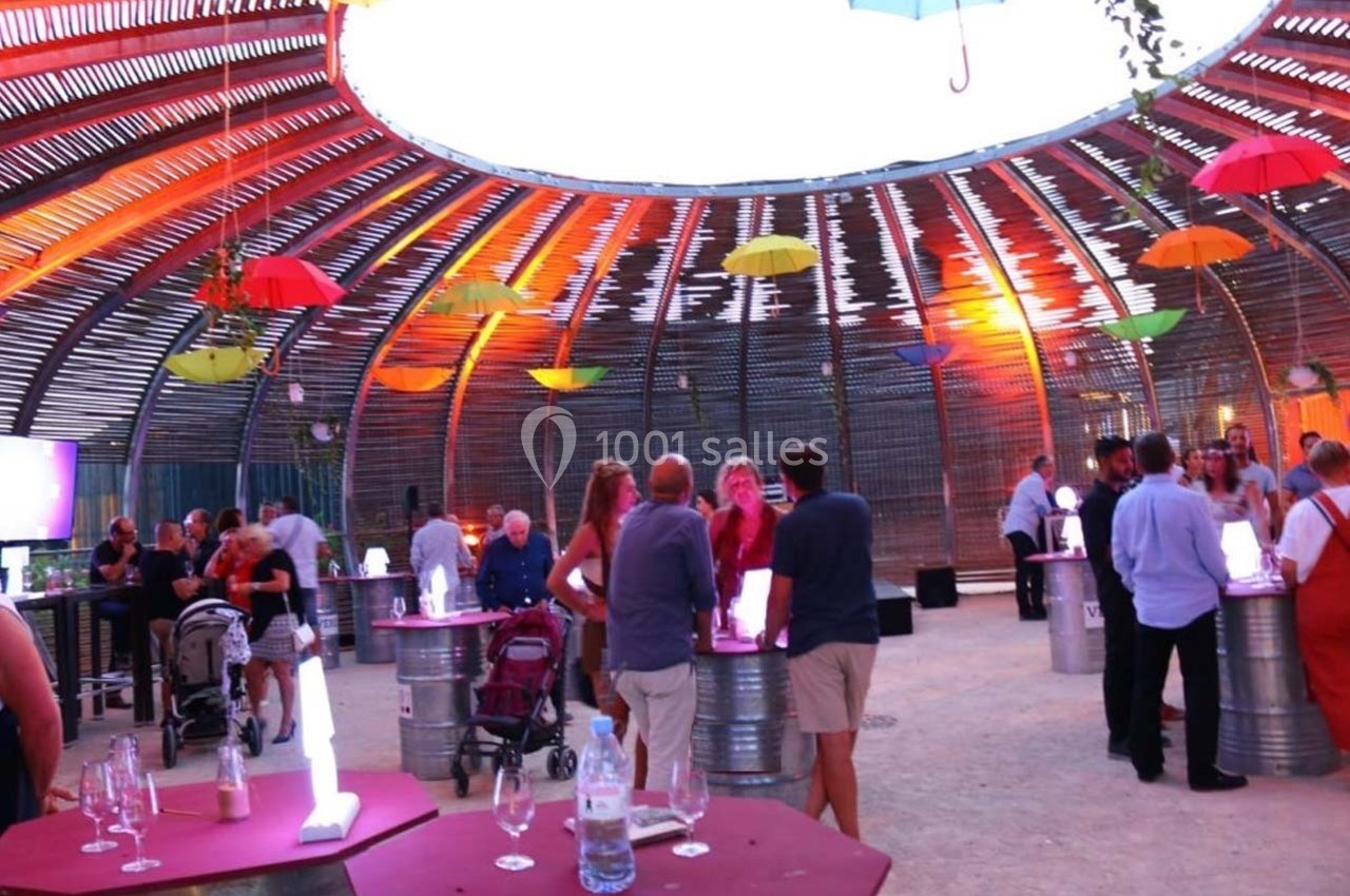 Des personnes discutent et se rassemblent dans un espace circulaire décoré de parasols colorés suspendus.