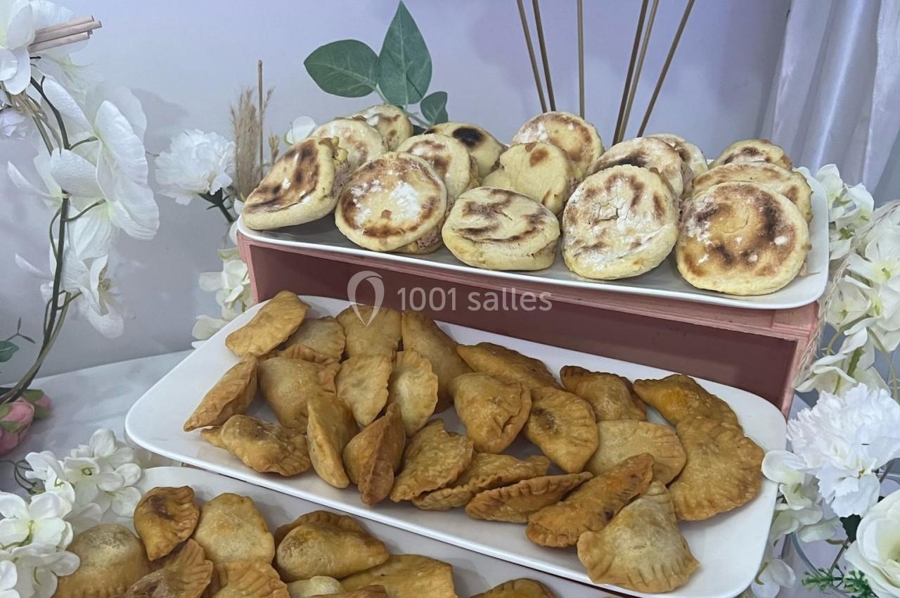 Assortiment de petits pains dorés et chaussons frits disposés sur des plateaux, entourés de fleurs décoratives.