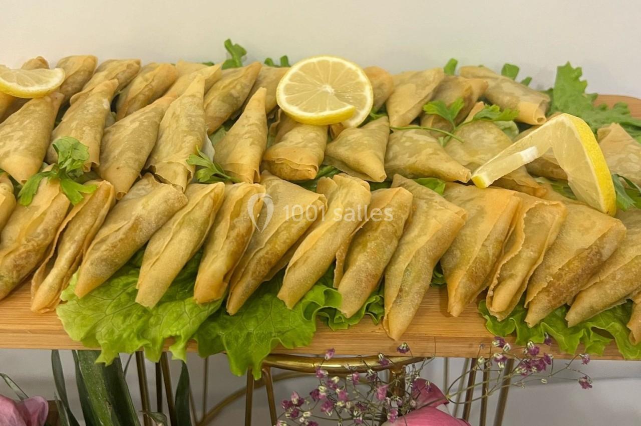 Assortiment de samoussas dorés disposés sur des feuilles de salade, décorés de quartiers de citron.