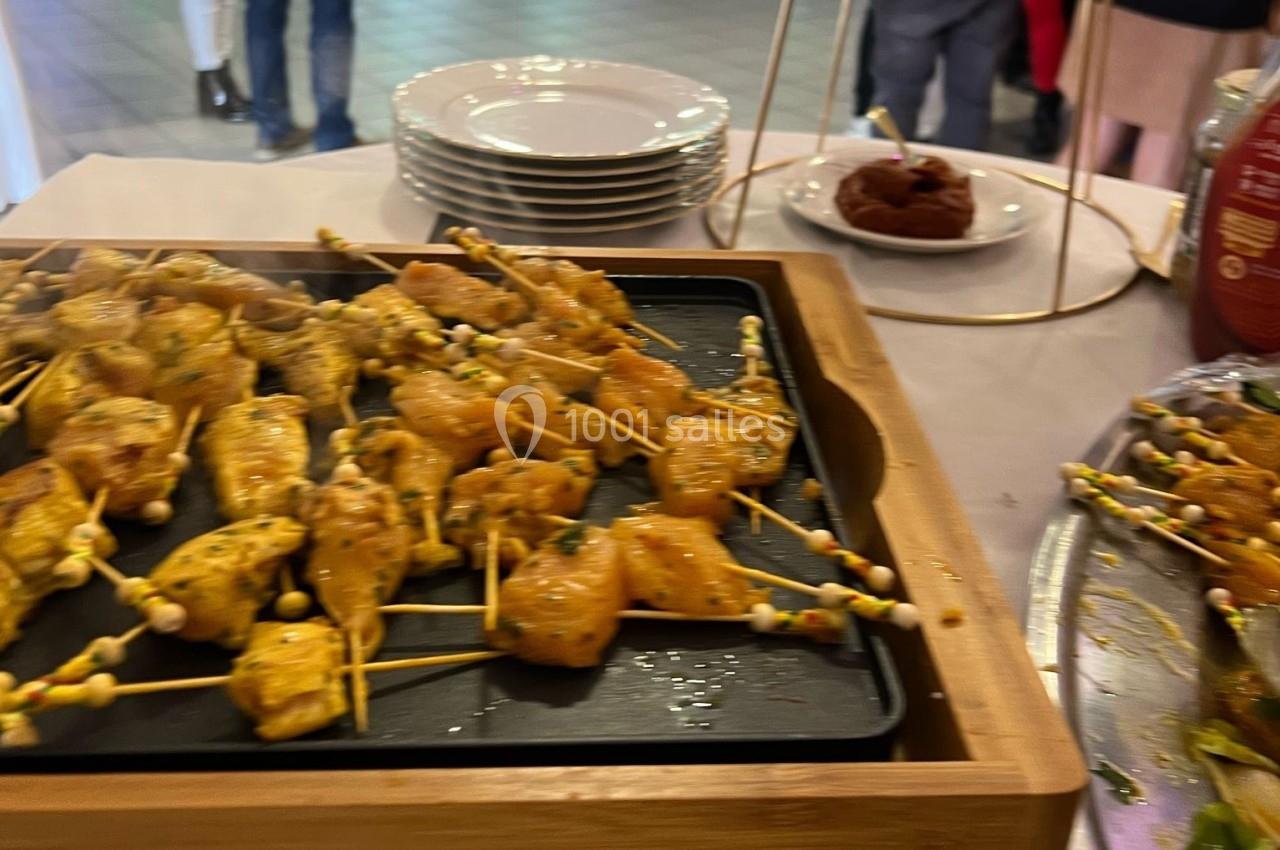 Brochettes de poulet marinées présentées sur un plateau, avec des assiettes empilées et des convives en arrière-plan.