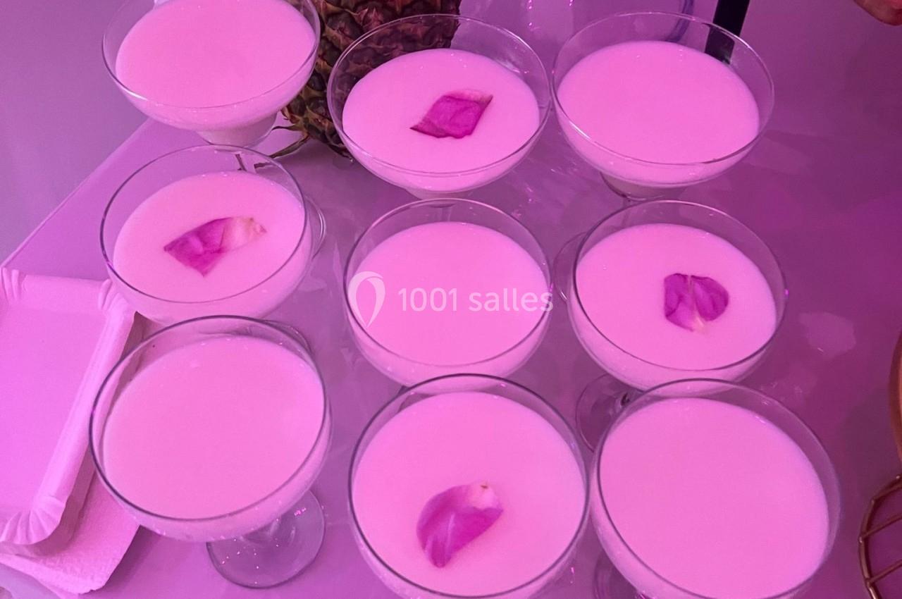Verres de cocktail rose pâle garnis de pétales de fleurs, disposés sur une table éclairée par une lumière violette.