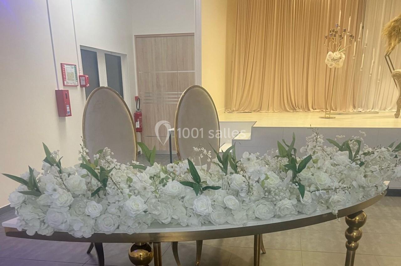 Deux chaises élégantes derrière une table ornée de fleurs blanches, devant un rideau beige et un chandelier.