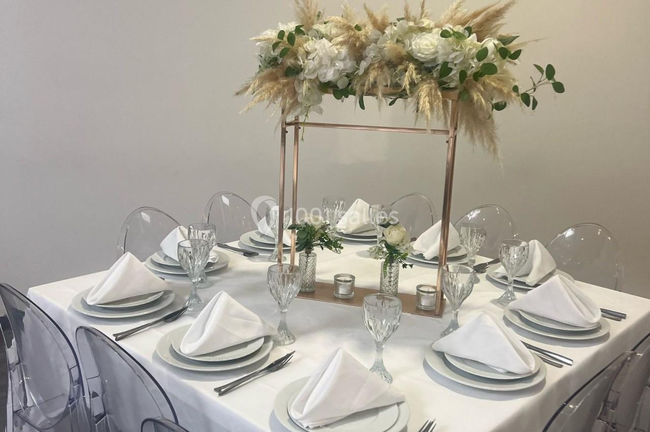 Table élégamment dressée avec des assiettes blanches, serviettes pliées, verres en cristal et centre de table floral.
