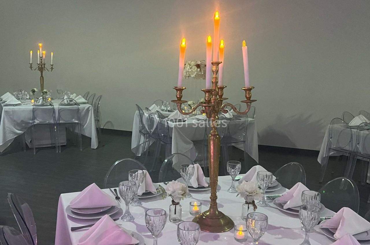 Salle de réception avec tables dressées, nappes blanches, chandeliers dorés et vaisselle élégante.