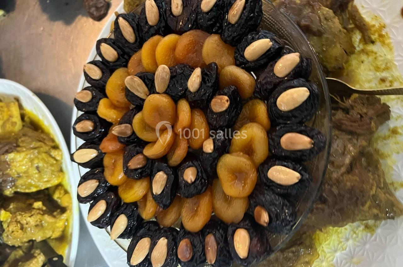 Plat de tajine décoré de pruneaux, abricots secs et amandes, présenté sur une table avec d'autres mets.