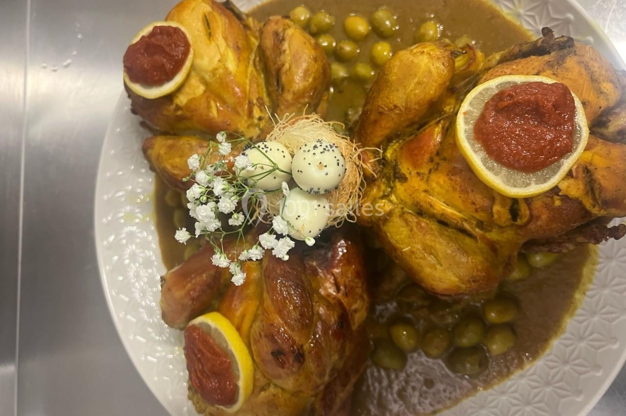 Poulets rôtis garnis de citron, sauce aux olives et décoration d'œufs et fleurs sur un plat blanc.