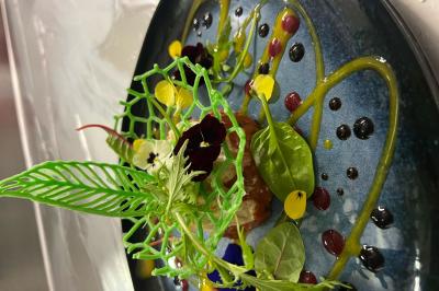 Macaron rouge garni de crème, framboise et groseilles, présenté sur une assiette blanche avec une cuillère dorée.