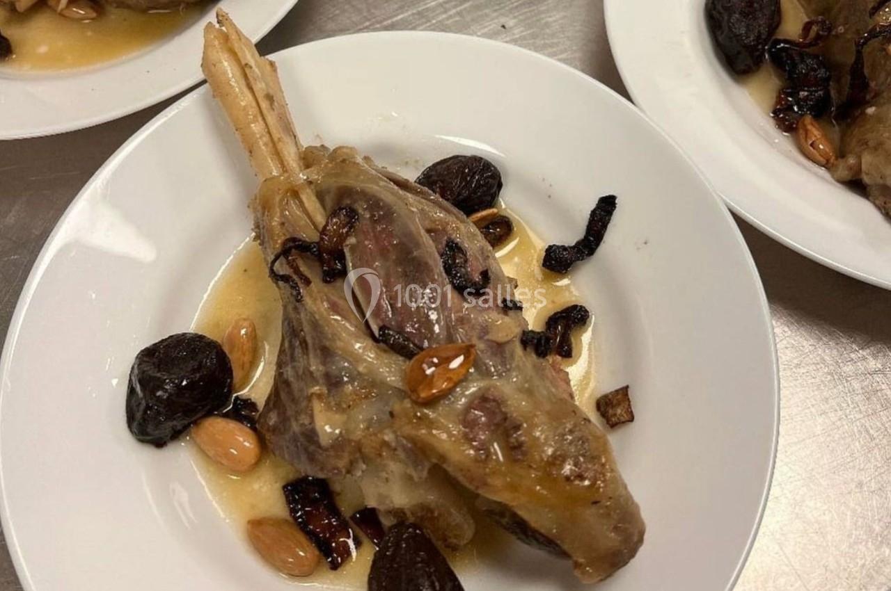 Plat de viande braisée avec sauce, amandes, pruneaux et morceaux d'oignons caramélisés, servi dans une assiette blanche.