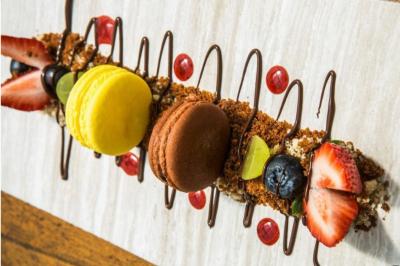 Macaron rouge garni de crème, framboise et groseilles, présenté sur une assiette blanche avec une cuillère dorée.