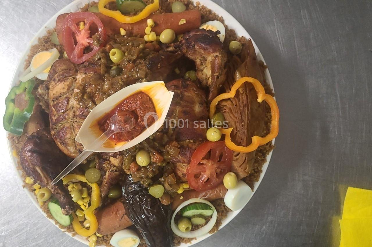 Plat de couscous garni de légumes, poulet rôti, œufs, olives, tranches de tomate et sauce rouge servie à part.