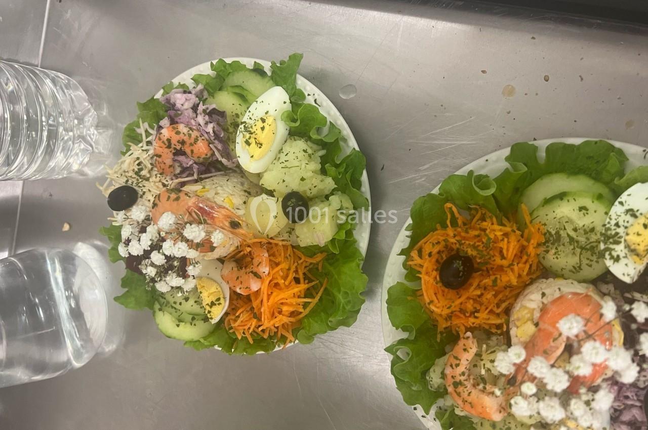 Assiettes de salade garnies de crevettes, œufs durs, crudités, olives noires et décorations florales.