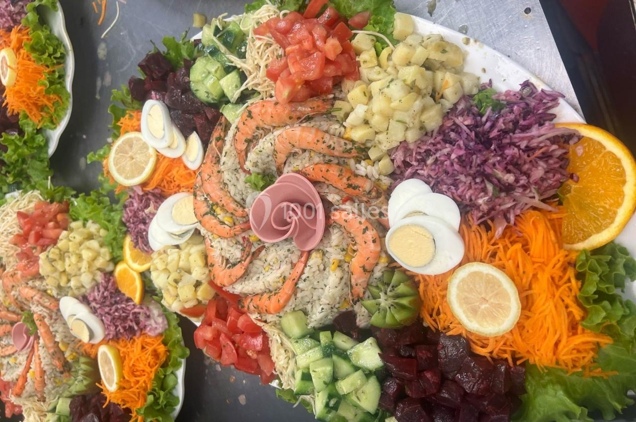 Assiette garnie de crudités variées, crevettes, œufs durs, agrumes et charcuterie, présentée sur un lit de salade.