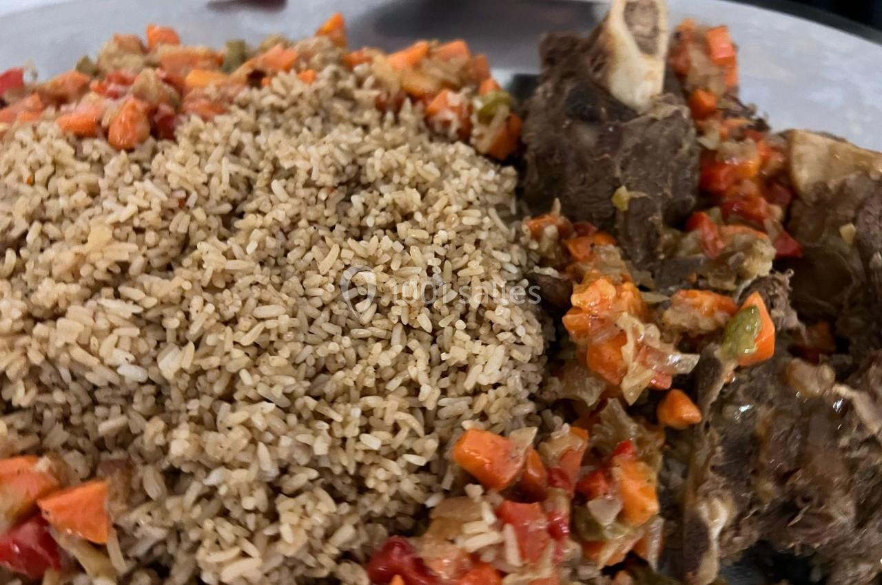 Assiette contenant du riz brun accompagné de morceaux de viande et de légumes cuits en sauce.