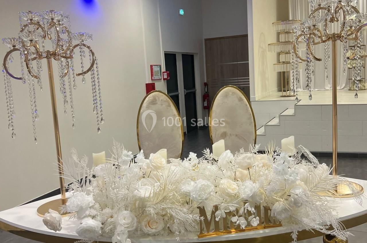 Décoration de table élégante avec fleurs blanches, chandeliers ornés de cristaux et deux chaises ovales dorées.