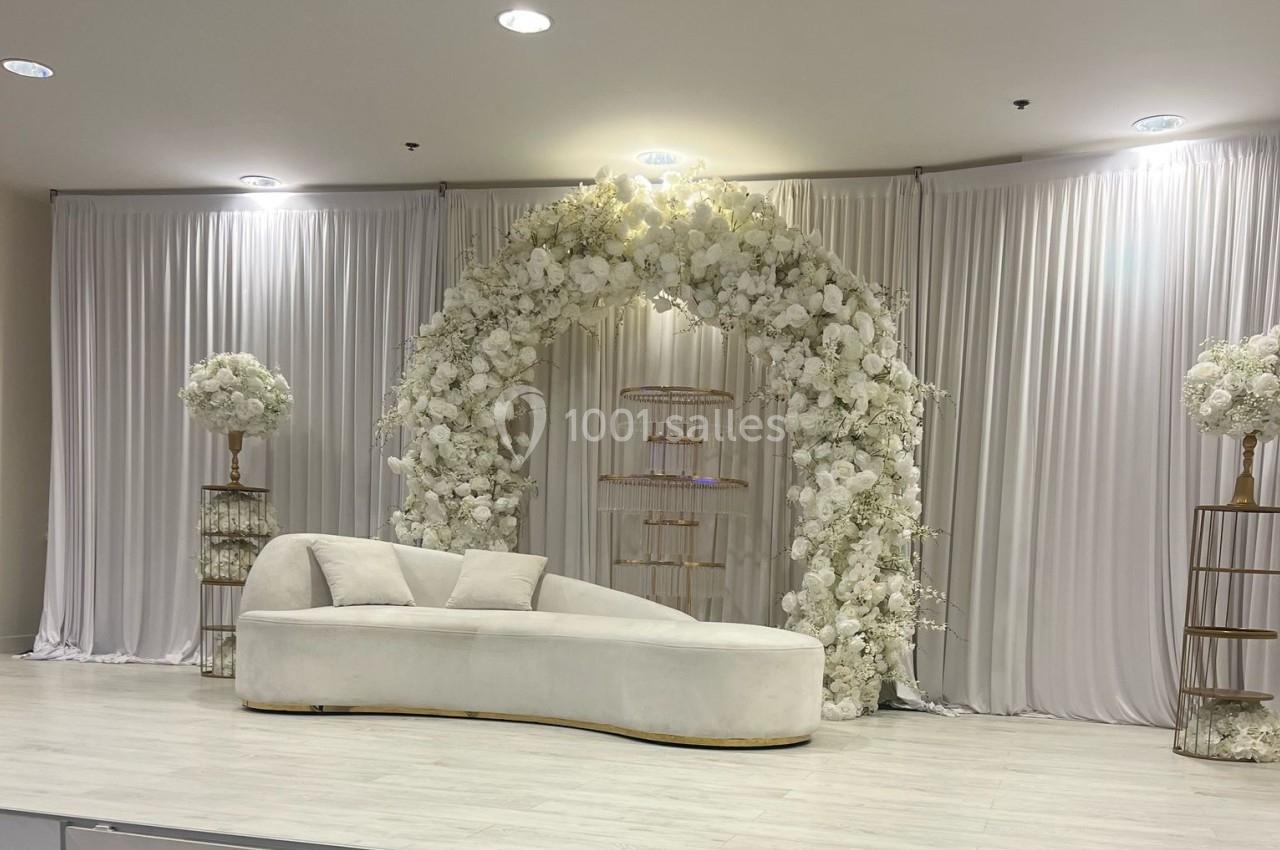 Canapé blanc devant une arche florale ornée de fleurs blanches, entouré de rideaux et de décorations élégantes.