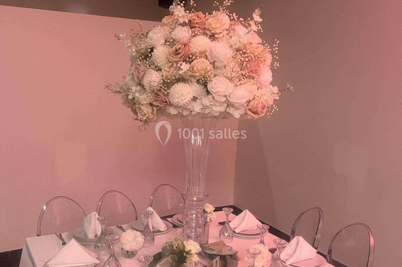 Centre de table floral avec des roses et des fleurs blanches dans un vase haut, entouré de couverts et de chaises…