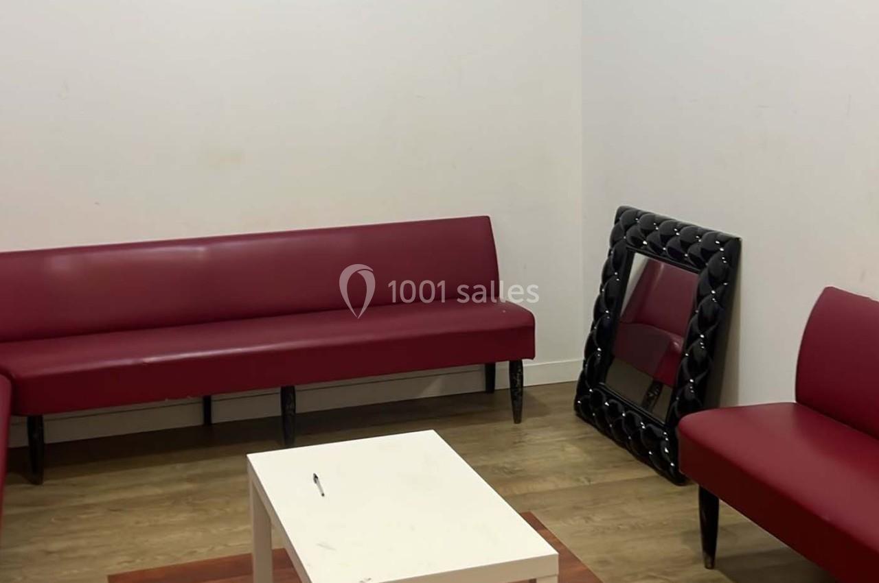 Salle avec murs blancs, deux banquettes rouges, une table basse blanche, un miroir posé au sol et un sol en bois.