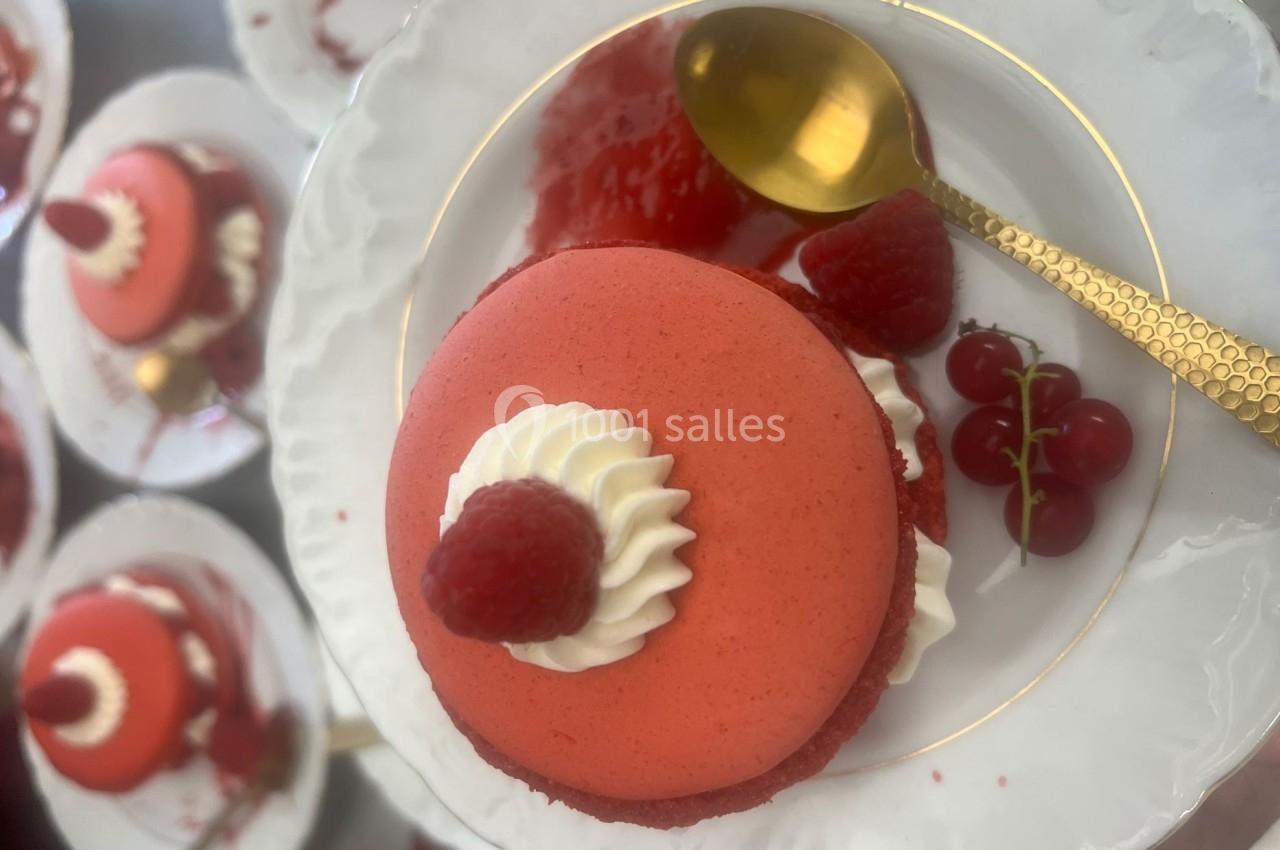 Macaron rouge garni de crème, framboise et groseilles, présenté sur une assiette blanche avec une cuillère dorée.
