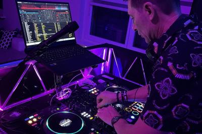 Un DJ mixe de la musique sur une table de mixage dans un environnement lumineux avec un écran affichant des visuels…